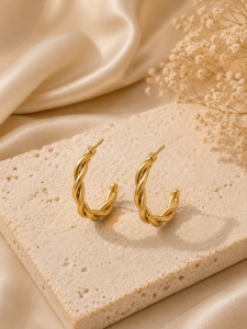 Elegant gold interwoven hoop earrings with braided detailing displayed on a neutral stone background.