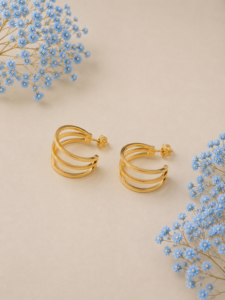Triple layer gold-plated hoop earrings with modern minimalist design on beige background with blue floral accents.