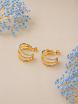 Triple layer gold-plated hoop earrings with modern minimalist design on beige background with blue floral accents.