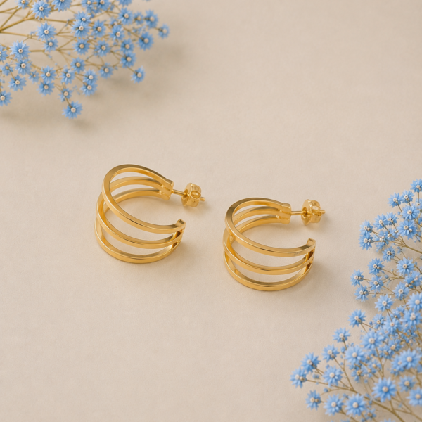 Triple layer gold-plated hoop earrings with modern minimalist design on beige background with blue floral accents.