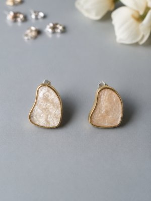 Abstract pearl resin stud earrings with gold-tone border and organic freeform design on a neutral background.