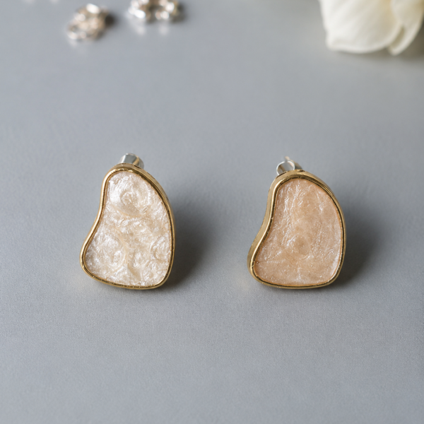 Abstract pearl resin stud earrings with gold-tone border and organic freeform design on a neutral background.
