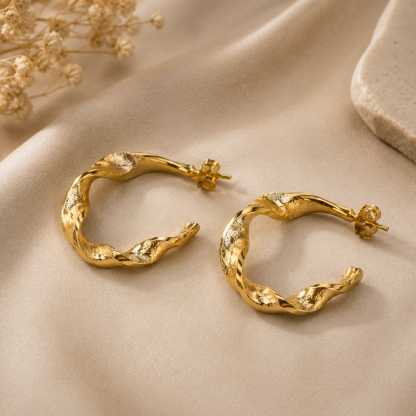 Twisted gold hoop earrings with organic sculptural design and polished gold-tone finish on a neutral background.