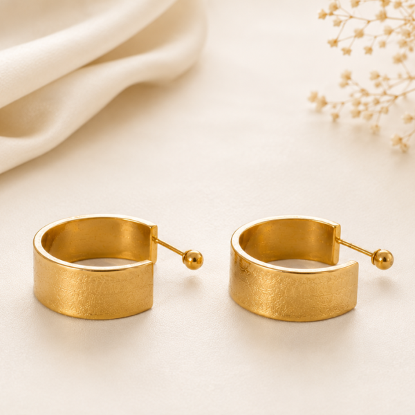 Gold wide cuff hoop earrings with brushed gold finish on a soft neutral background.