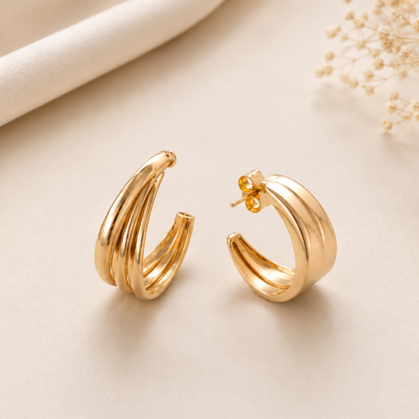 Gold triple layer hoop earrings with polished finish displayed on a soft neutral luxury background.