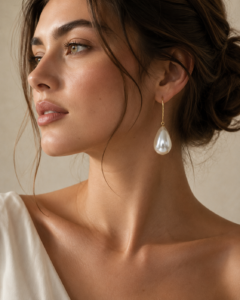 Foreign fashion model wearing elegant pearl teardrop drop earrings with gold-tone hook design in a luxury studio photoshoot.
