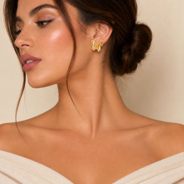 Woman wearing elegant gold butterfly stud earrings with textured wing detailing and a polished finish.
