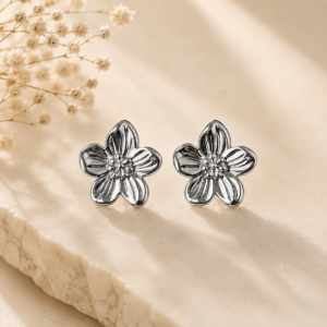 Silver blossom flower stud earrings with polished floral design displayed on a beige stone surface.