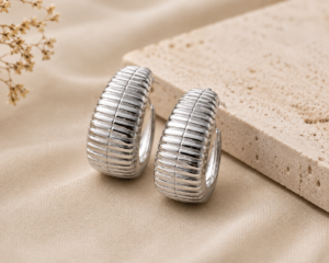 Silver ribbed hoop earrings with a polished finish displayed on a neutral beige background.