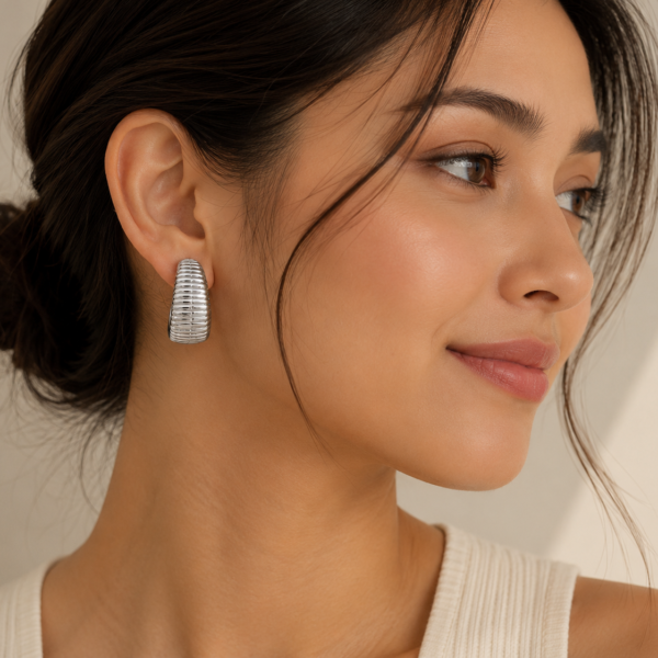 Silver ribbed hoop earrings with a polished finish displayed on a neutral beige background.