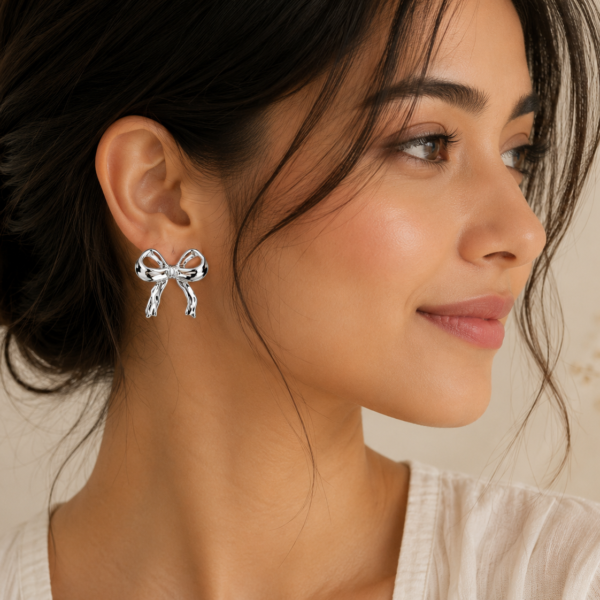Elegant silver bow-shaped stud earrings with a polished mirror finish displayed on a neutral beige background.