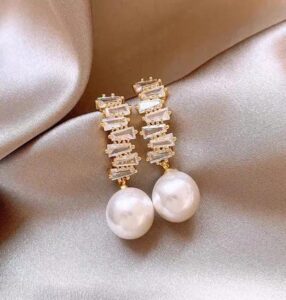 Woman wearing elegant gold pearl drop earrings with a modern gold-plated design and white pearl accents.