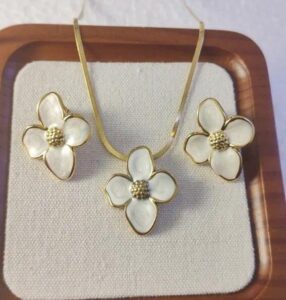 cream color floral enamel jewelry set with gold-tone flower pendant necklace and matching stud earrings displayed on a luxury beige background