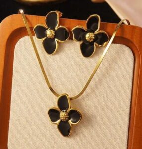 Black floral enamel jewelry set with gold-tone flower pendant necklace and matching stud earrings displayed on a luxury beige background