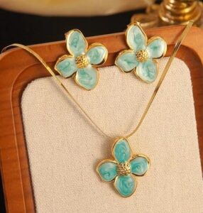 Mint Green floral enamel jewelry set with gold-tone flower pendant necklace and matching stud earrings displayed on a luxury beige background