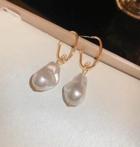 Woman wearing elegant gold pearl drop earrings with a modern gold-plated design and white pearl accents.